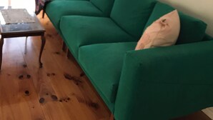 A green sofa with a white pillow, a wooden coffee table, and a framed picture on the wall.