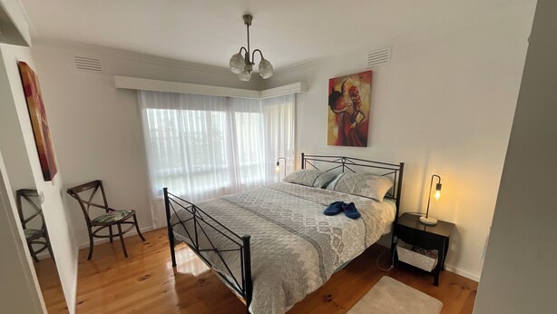 A bedroom with a bed, a chair, a bedside table with a lamp, and a painting on the wall.