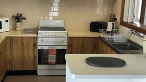 A compact kitchen with a microwave, stove, toaster, sink, and a dish rack.