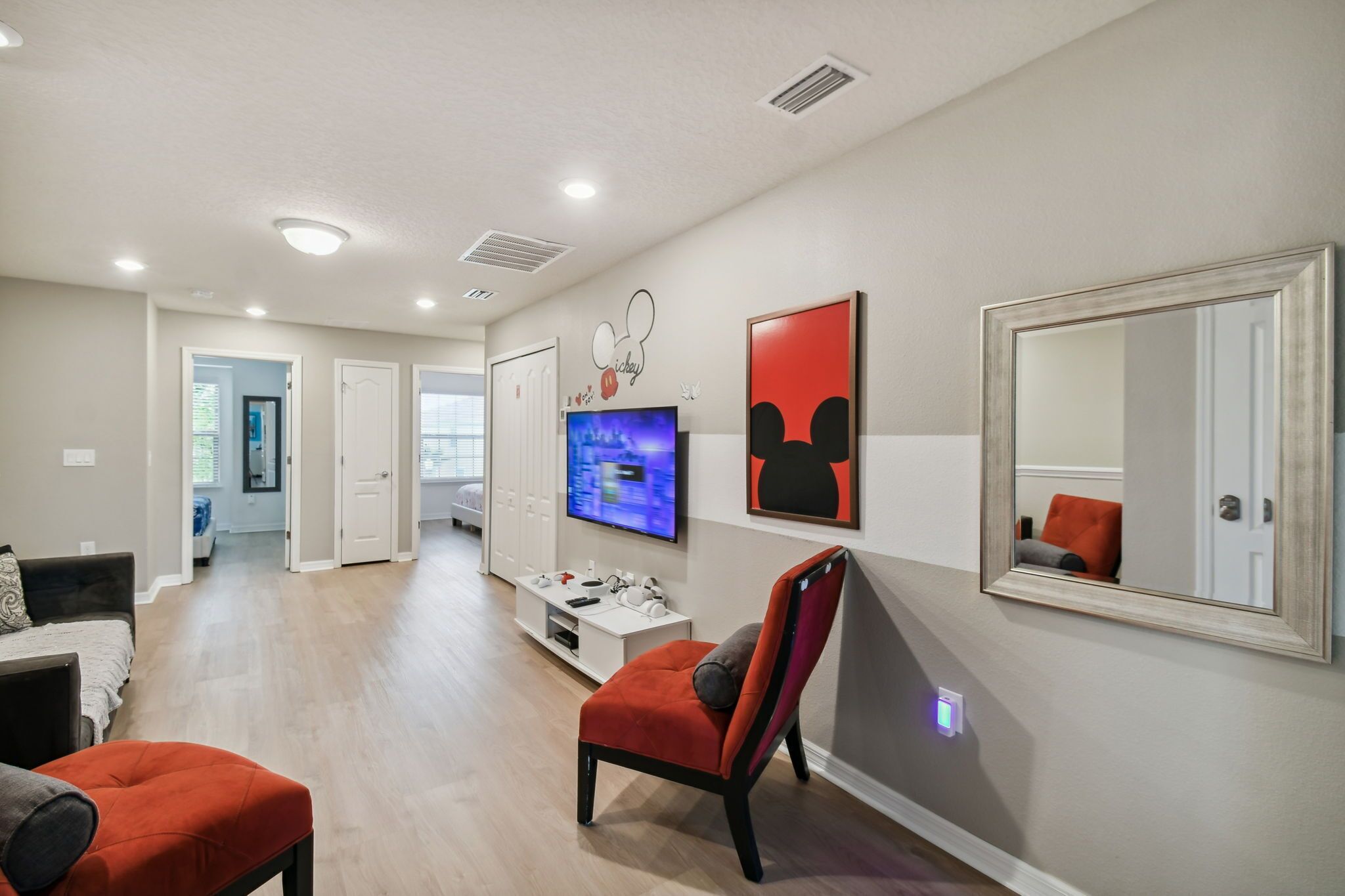 A modern living room with a flat-screen TV, a red chair, and a large mirror.