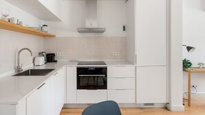 Eine moderne Küche mit weißen Schränken, einem eingebauten Backofen, einer Edelstahl-Dunstabzugshaube und einem Holzregal über der Spüle.