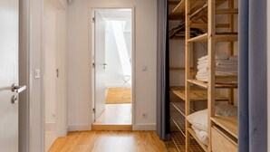 Ein Flur, der zu einem Schlafzimmer mit Holzboden, einem Kleiderschrank mit Regalen und einer Tür zu einem anderen Raum führt.
