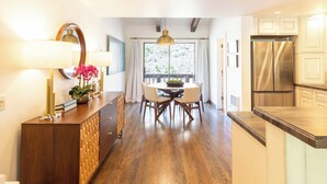 A modern kitchen with wooden flooring, a dining area with a round table and chairs, a large window with curtains, and a stainless steel refrigerator. - Val D Sol Retreat: Perfect Sun Valley Base (Sun Valley)