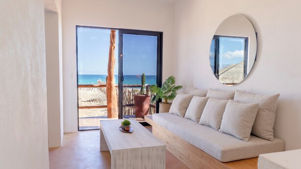 Een moderne woonkamer met een bank, een salontafel en een groot raam met uitzicht op een strand.