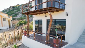 Een modern huis met een houten terras, plantenpotten en uitzicht op het strand.
