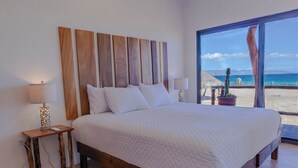 Een slaapkamer met een groot bed, een houten hoofdeinde, bedlampen en uitzicht op het strand.