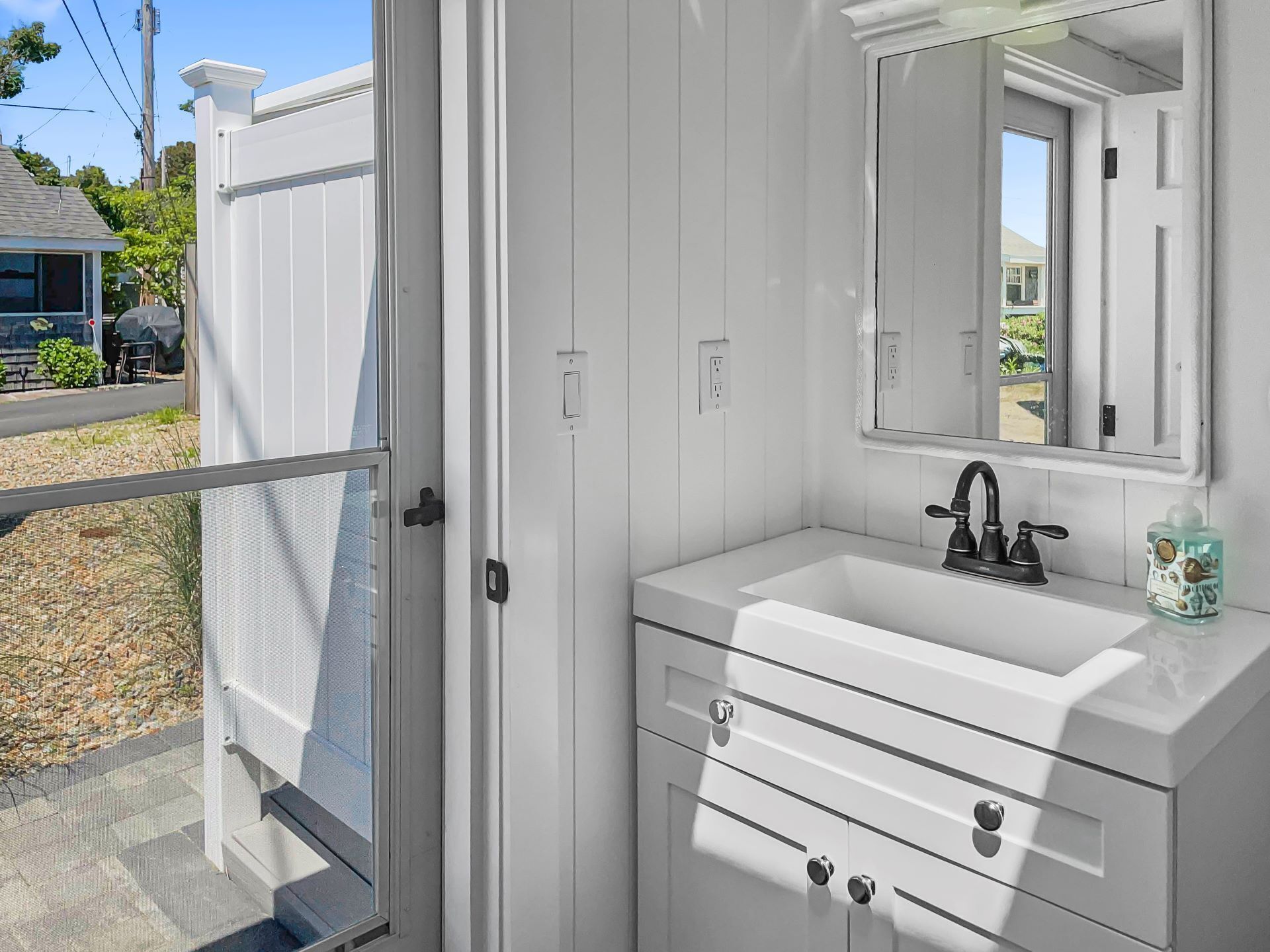 Un baño blanco con un espejo grande, un lavamanos y una ventana.