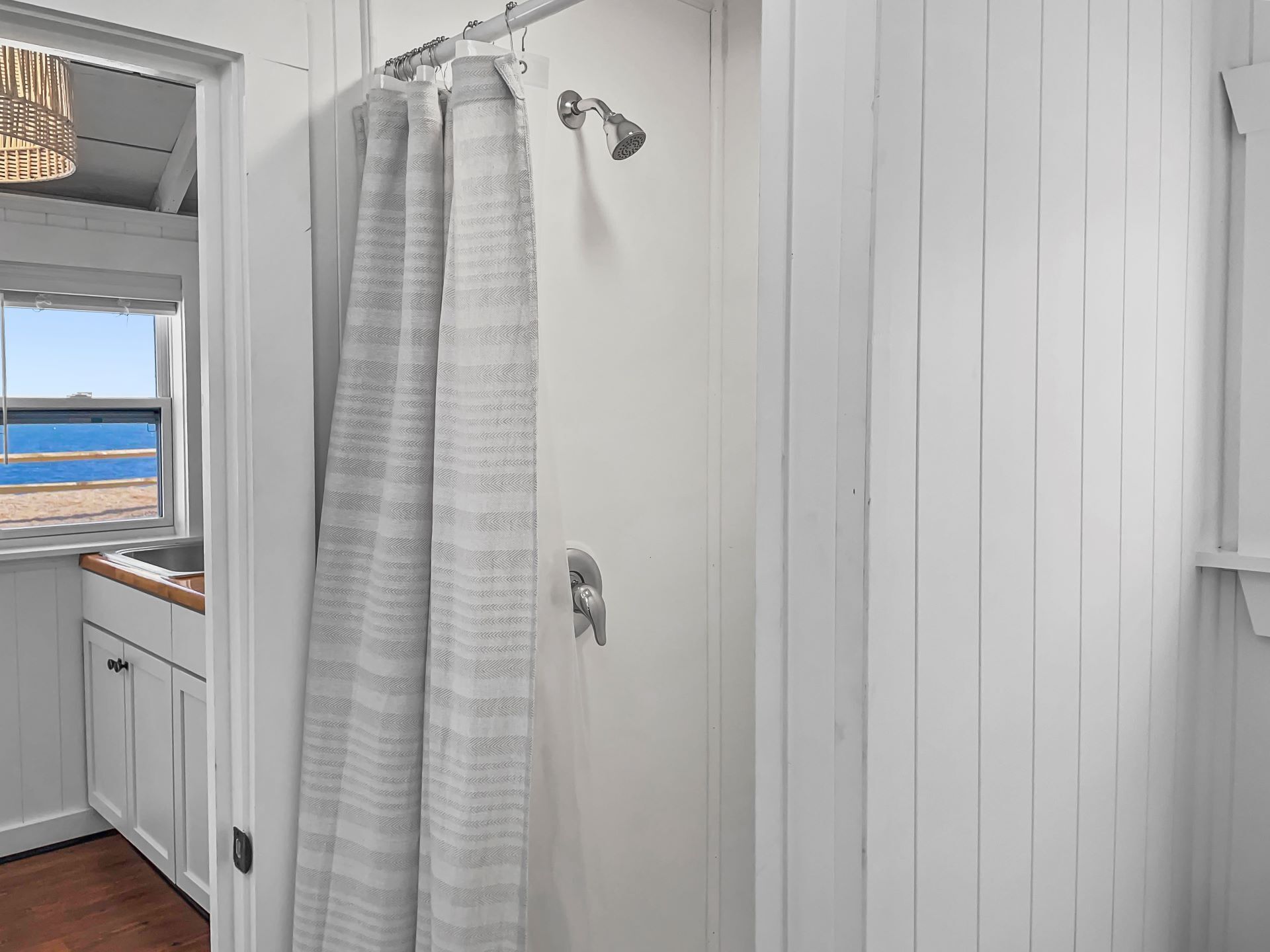 A bathroom with a shower curtain, a window with a view of the beach, and a towel rack.