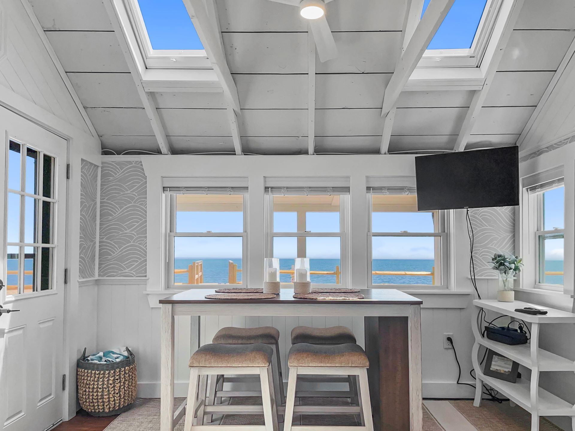 A kitchen with a view of the ocean, a ceiling fan, and a TV mounted on the wall.