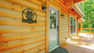 A wooden cabin with a raccoon-themed sign, a door, and a deck.