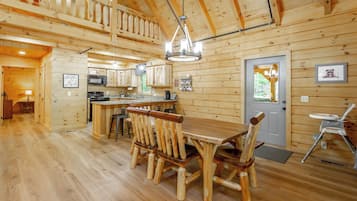 A wooden cabin interior with a dining area, kitchen, and a balcony.