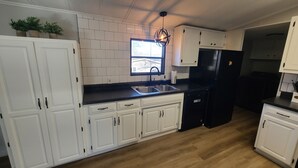 Une cuisine moderne avec des meubles blancs, un réfrigérateur noir et une fenêtre au-dessus de l’évier.