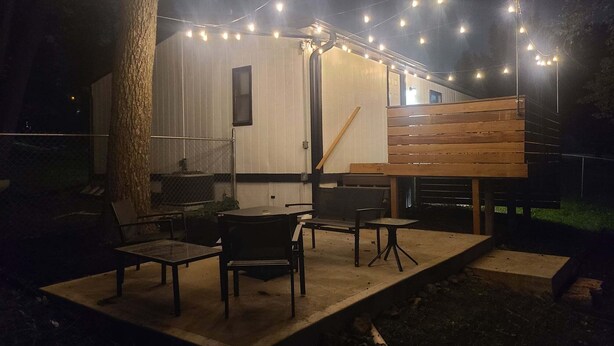 Un espace extérieur aménagé en patio, avec une table et des chaises, des guirlandes lumineuses et un banc en bois.
