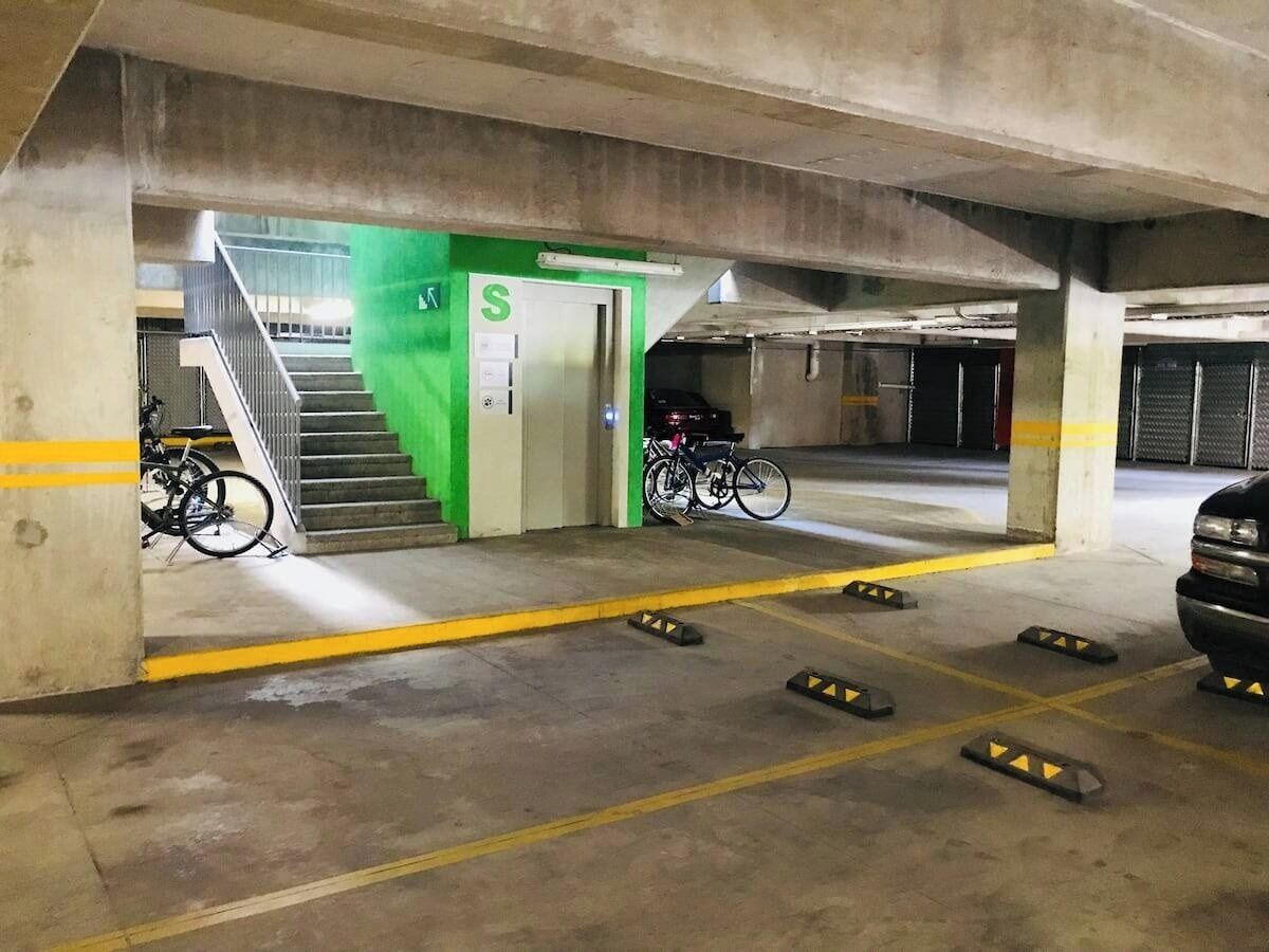 Un parking avec des piliers en béton, des lignes jaunes et un panneau de signalisation vert indiquant la sortie.