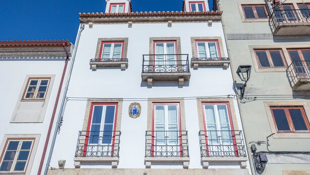 Un immeuble à plusieurs étages, doté de balcons, de fenêtres à cadre rouge et d’un toit recouvert de tuiles.