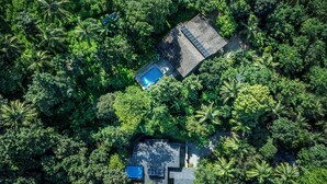 An aerial view of a secluded resort with a swimming pool, a covered patio, and lush tropical vegetation.