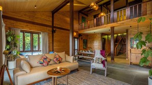 A spacious living area with a sofa, coffee table, and a dining table. A staircase leads to an upper level with a balcony.