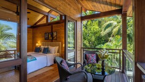 A wooden cabin with a balcony, a bed with pillows, and a table with a vase.