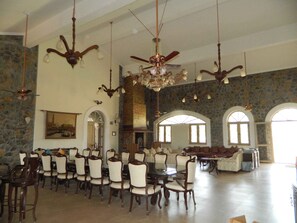 A spacious lobby with a high ceiling, multiple chandeliers, and a stone wall. There are several dining tables and chairs arranged for guests.