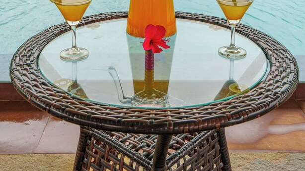 Mesa de vidro com um jarro e duas taças de martini, colocada junto a uma piscina com vista para as montanhas.