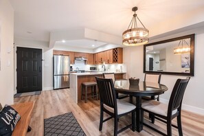 A modern kitchen with a central island, stainless steel appliances, and a dining area with a round table and chairs. - Walk to Blackcomb | Complex hot tub | BBQ (Whistler)