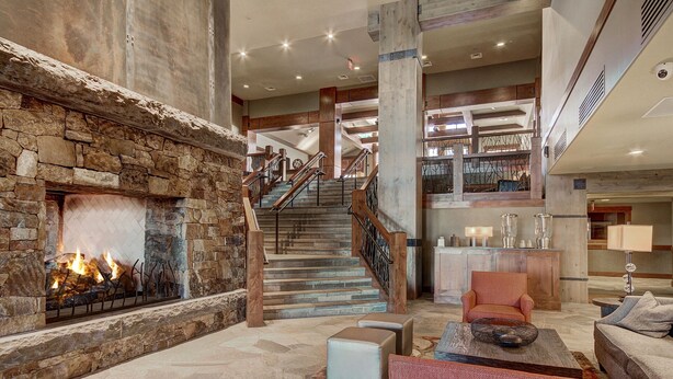 A spacious lobby with a stone fireplace, a staircase, and a seating area with a coffee table and ottomans.