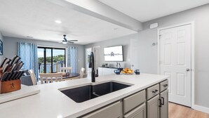 Cozinha moderna com uma ilha grande, armários brancos e vista para o exterior.
