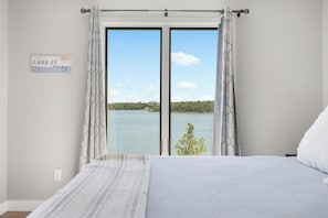 A bedroom with a large window overlooking a lake, a bed with white bedding, and a sign on the wall.