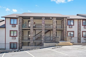 A multi-story building with a central entrance, balconies, and a parking lot in front.