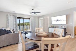 A modern living room with a round dining table, a sofa, and a balcony with a view.