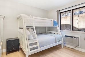 A bunk bed with a ladder, a bedside table, and a window with a view of the outside.