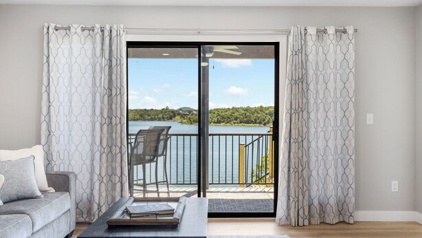 Sala de estar moderna com sofá cinza, mesa de centro preta e vista para um lago através de uma porta de vidro.