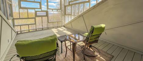A sunroom with a view of trees and mountains, furnished with green chairs and a table.