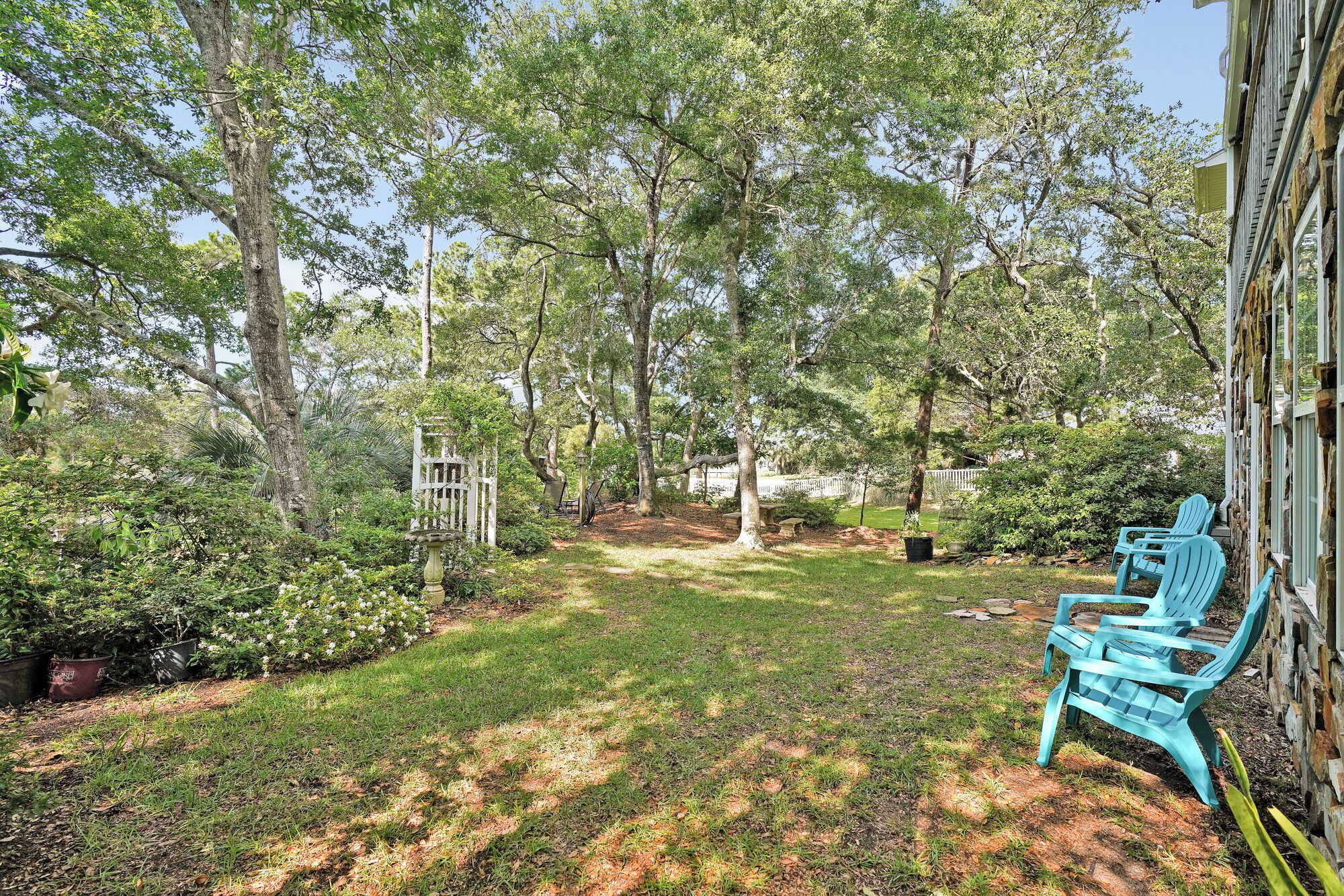 A backyard with a lawn, a wooden gazebo, and a blue chair.