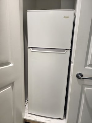 A white Danby refrigerator in a narrow hallway with a door handle on the right.