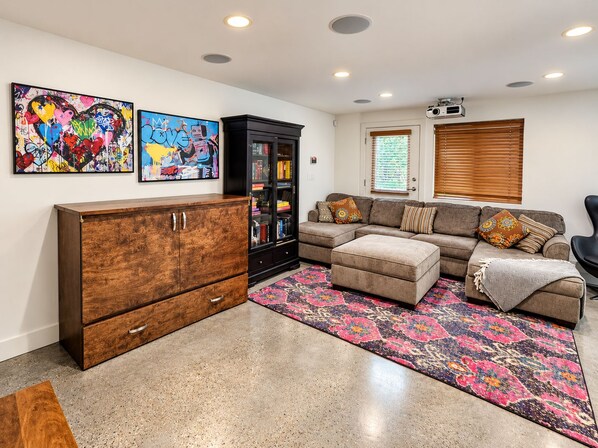 A living room with a sectional sofa, a wooden cabinet, and colorful artwork on the wall. - 2 bedroom Guest Suite with Pool & Sauna access (West Vancouver)