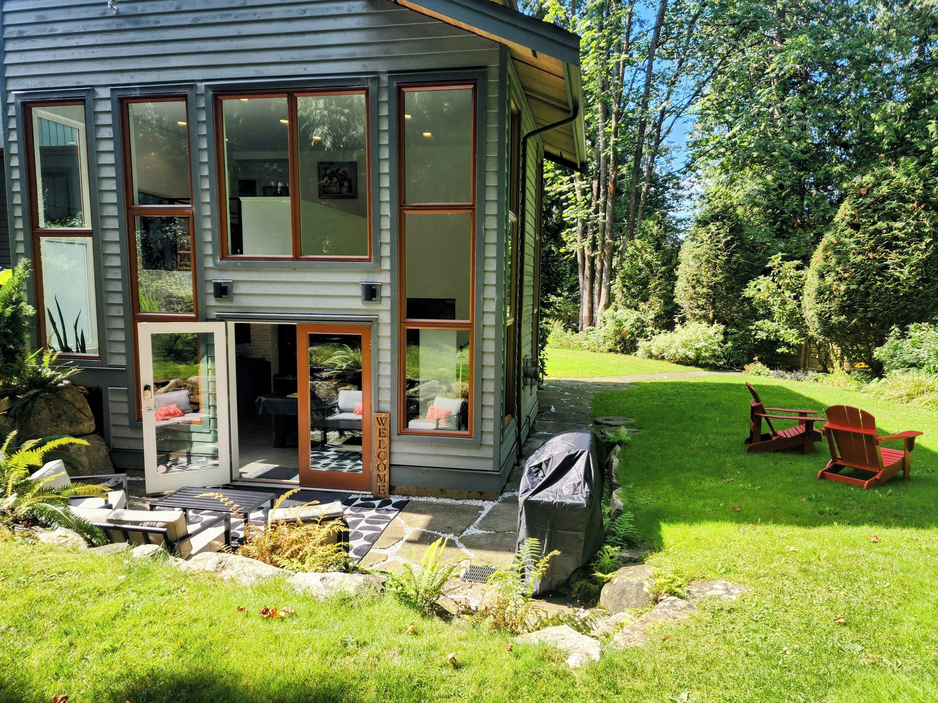 Une maison moderne à deux étages, dotée de grandes fenêtres, d’un chemin en pierre menant à l’entrée et d’une pelouse bien entretenue agrémentée de mobilier d’extérieur.