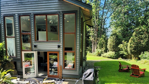 Una casa moderna de dos pisos con amplios ventanales, un sendero de piedra que conduce a la entrada y un césped cuidado con muebles de exterior.