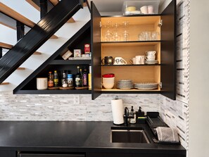 A kitchen with a black countertop, a built-in shelf with glassware, and a tiled backsplash. - 2 bedroom Guest Suite with Pool & Sauna access (West Vancouver)
