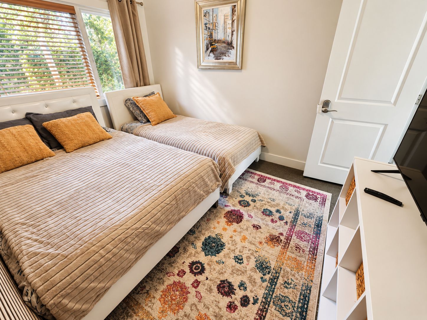 A bedroom with two beds, a patterned rug, a painting, and a television on a stand.