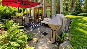 A patio with outdoor furniture, a covered grill, and a red umbrella.