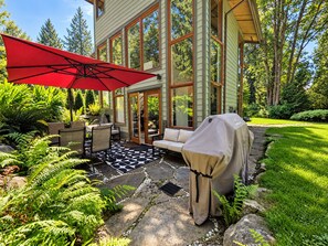 Une terrasse avec des meubles d’extérieur, un barbecue couvert et un parasol rouge.