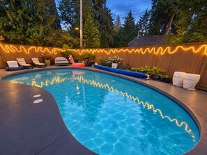A swimming pool with a wavy light pattern on the edge, surrounded by lounge chairs and potted plants.