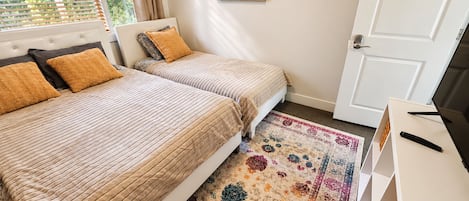 Ein Schlafzimmer mit zwei Betten, einem gemusterten Teppich, einem Gemälde und einem Fernseher auf einem Schrank.
