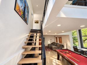 Un interior moderno con una escalera de madera, una mesa de billar y una sala de estar con sofá.