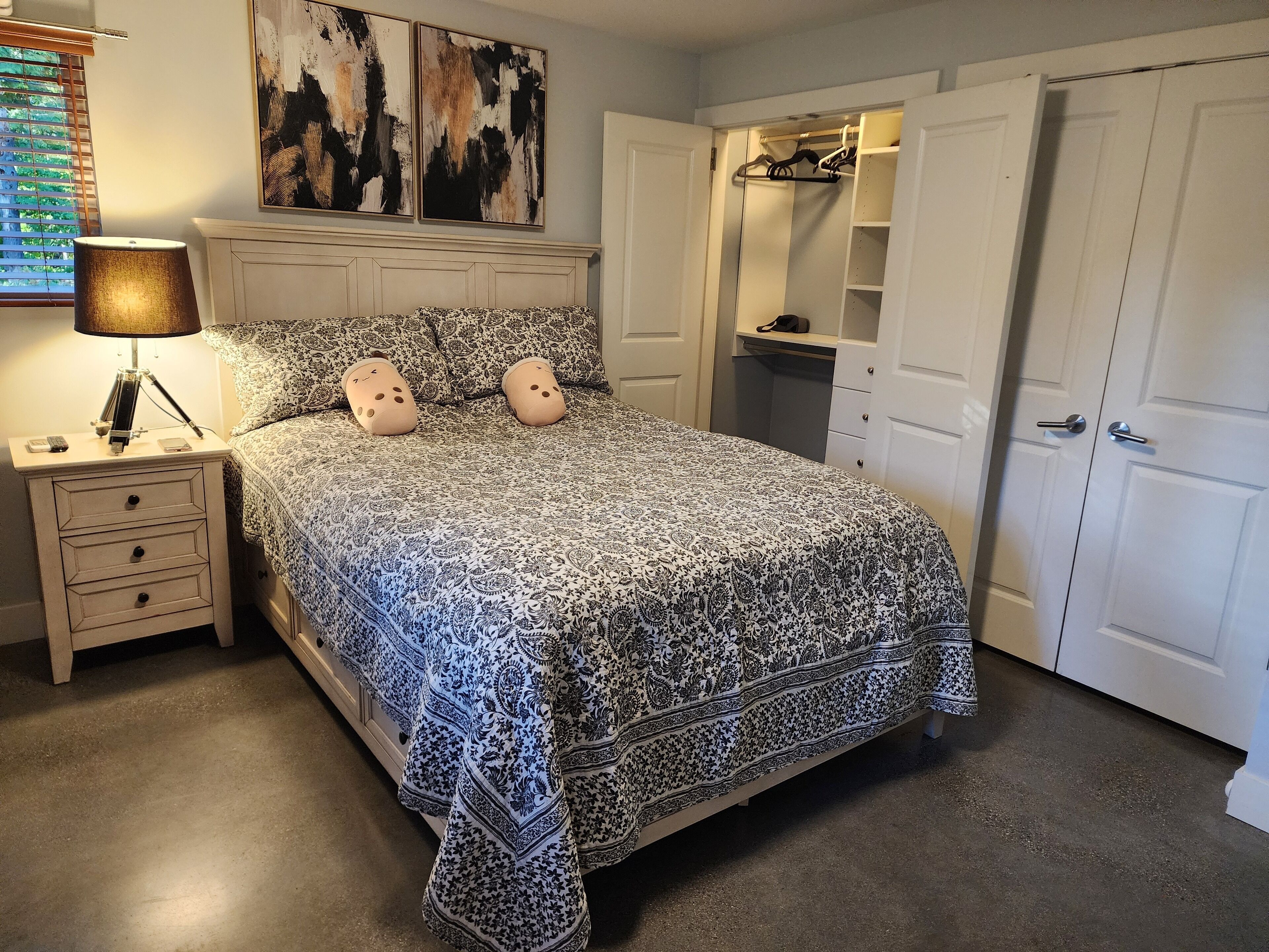 A bedroom with a patterned bedspread, a bedside lamp, a nightstand, and a closet with hanging space.