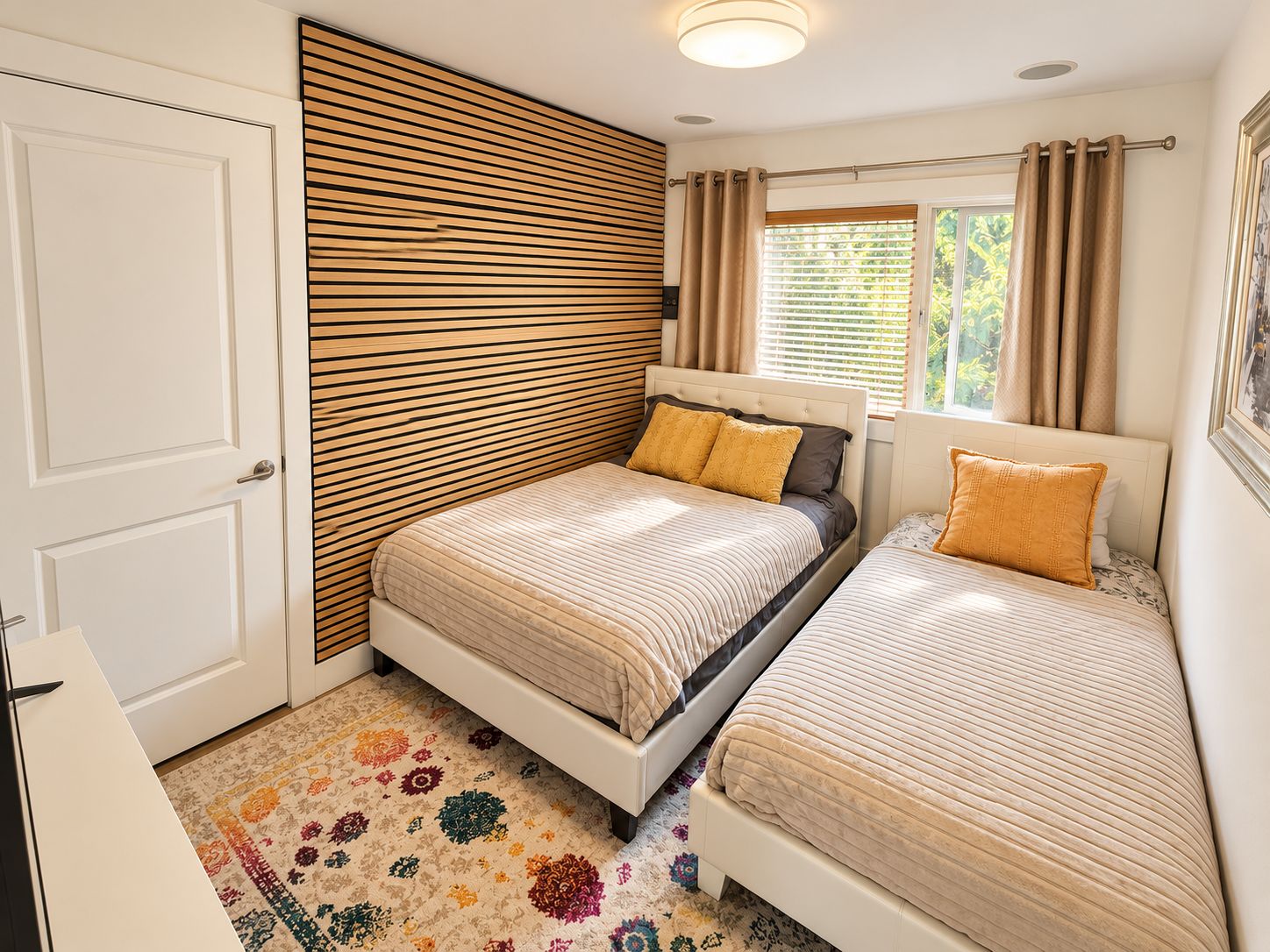 A bedroom with two beds, a wooden slat wall, a window with curtains, and a patterned rug.