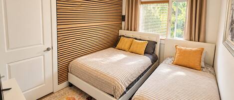 Une chambre avec deux lits, un mur avec des lambris en bois, une fenêtre avec des rideaux et un tapis à motifs.