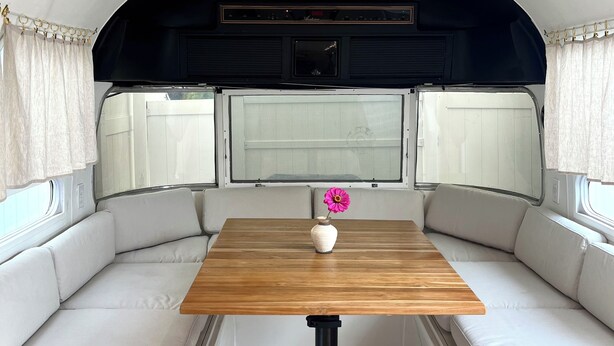 A compact RV interior with a wooden table, cushioned seating, and a window with curtains. - Englewood retreat just 12 minutes from the beach (Englewood)