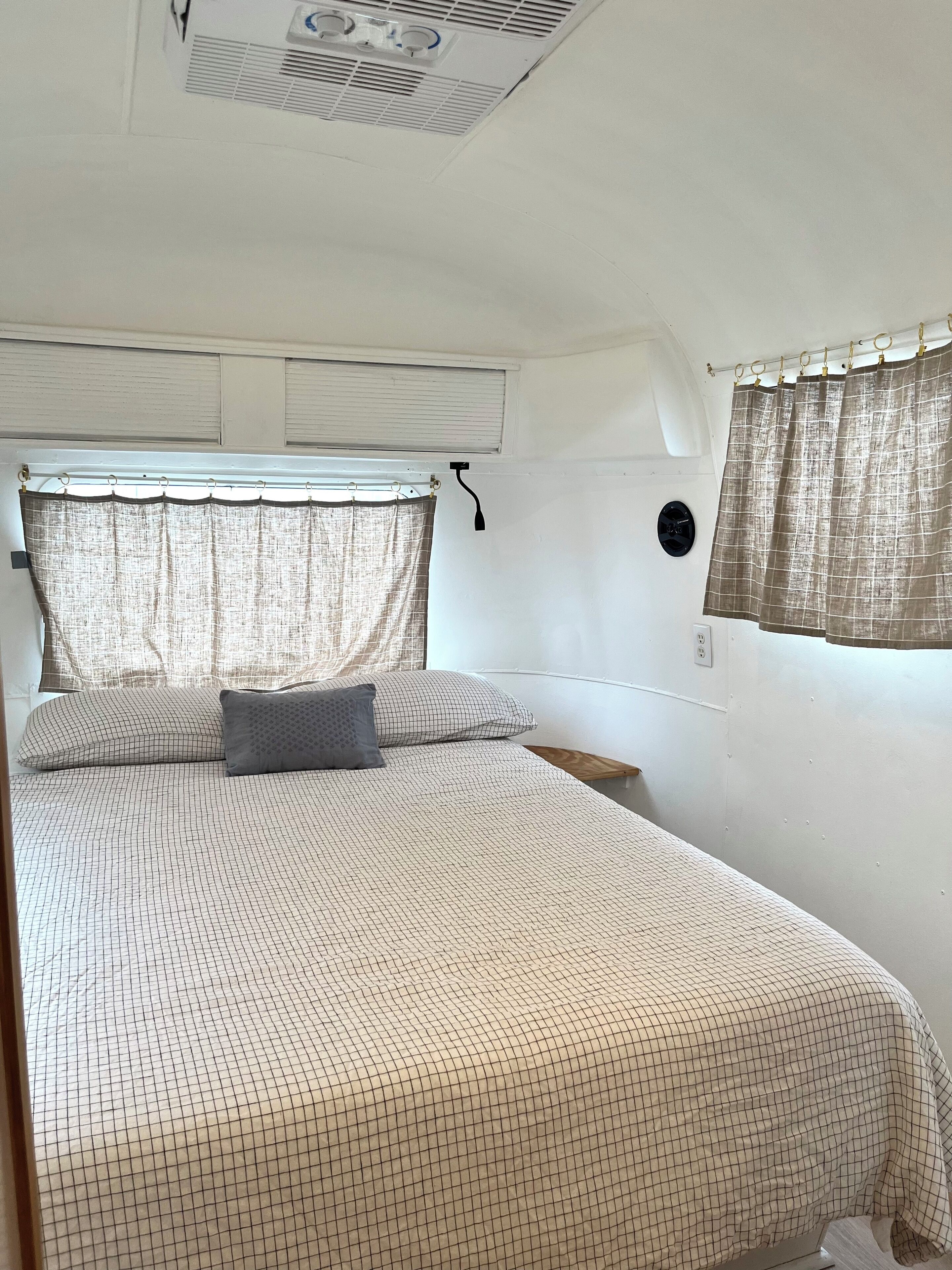 Una camera da letto con un letto, una finestra con tende, una bocchetta d'aria sul soffitto e una presa a muro.